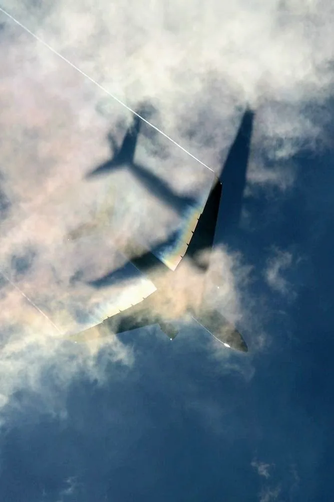 An aeroplane flying through clouds, its shadow cast on the cloud below